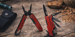 Мультитул Hank TM Discover червоно-чорний з відкритими інструментами на дерев’яній поверхні