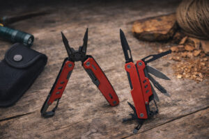 Мультитул Hank TM Discover червоно-чорний з відкритими інструментами на дерев’яній поверхні