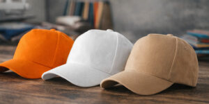 Кепки 5P Malfini у трьох кольорах (помаранчева, біла, бежева) на дерев’яній поверхні