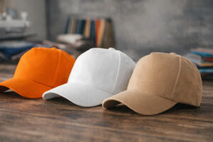 Кепки 5P Malfini у трьох кольорах (помаранчева, біла, бежева) на дерев’яній поверхні