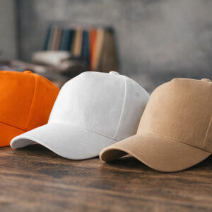 Кепки 5P Malfini у трьох кольорах (помаранчева, біла, бежева) на дерев’яній поверхні