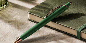 Ручка кулькова металева Diamond темно-зелена з золотими деталями на столі поруч із блокнотом